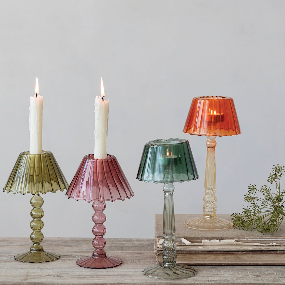 Four colored glass lampshade candle holders with lit candles arranged on a wooden table.