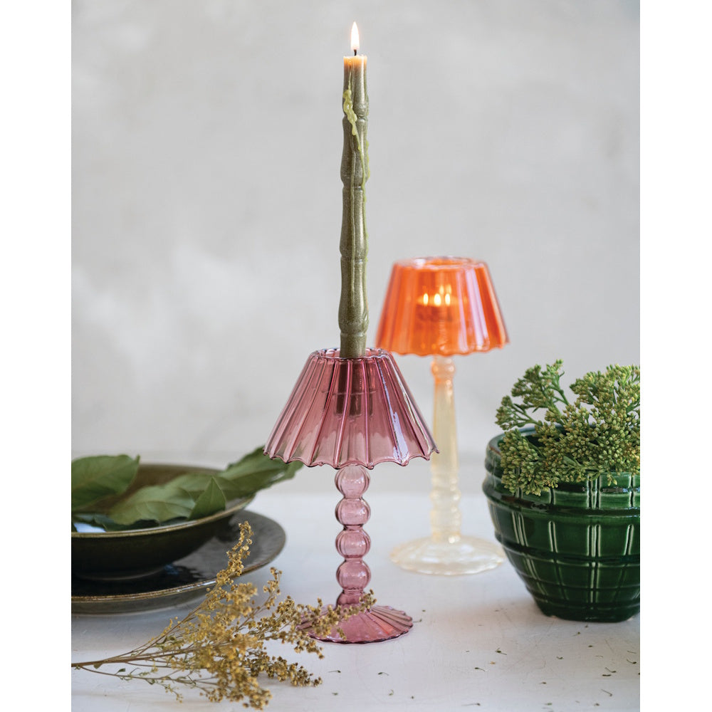 Pink glass lampshade candle holder with a lit green taper candle next to an orange candle holder.