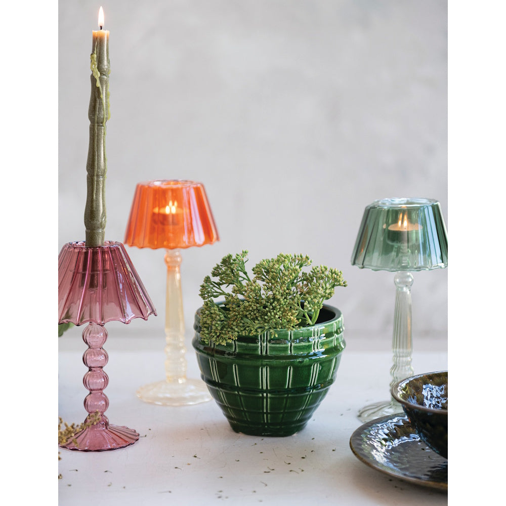Three colored glass lampshade candle holders with lit candles and a potted plant on a table.