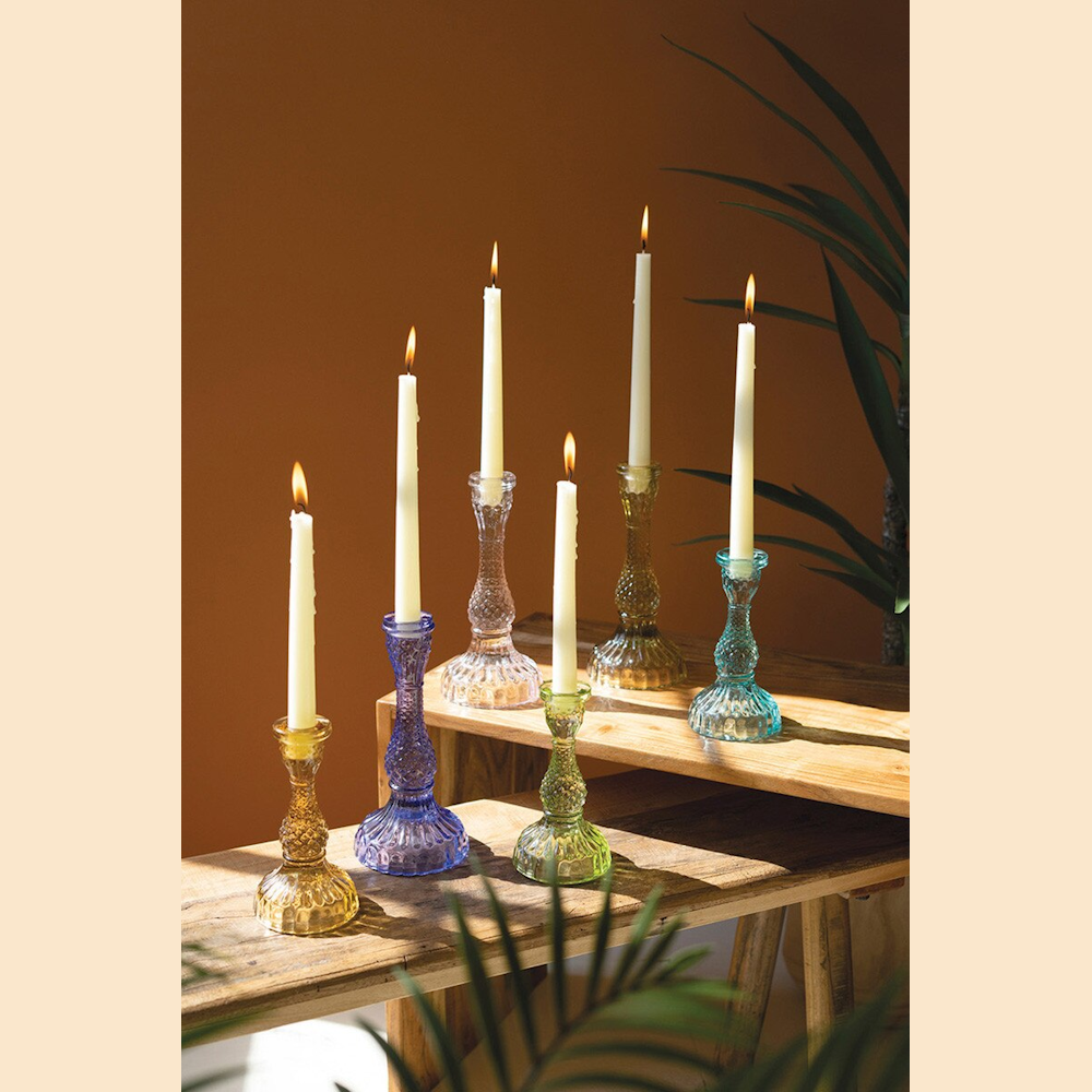 Colorful vintage-style textured glass taper candle holders with lit white candles on a wooden bench.