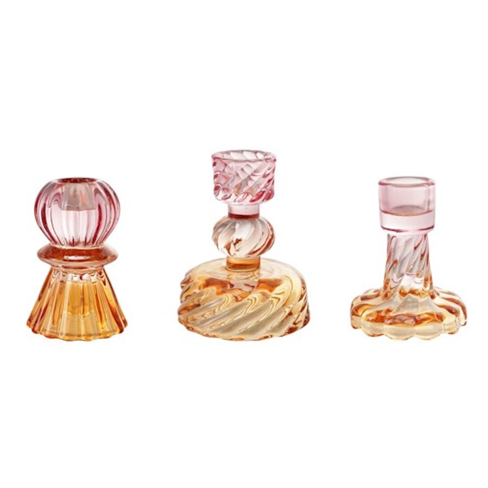 Three small, ribbed glass taper candle holders in varying shapes with a pink and amber gradient on a white background.