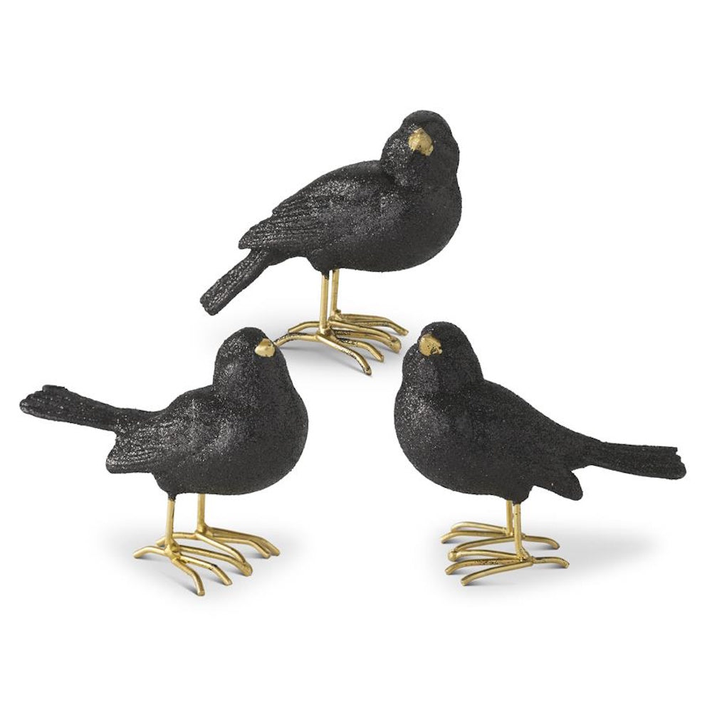 Three glittery black resin bird figurines with gold beaks and feet on a white background.