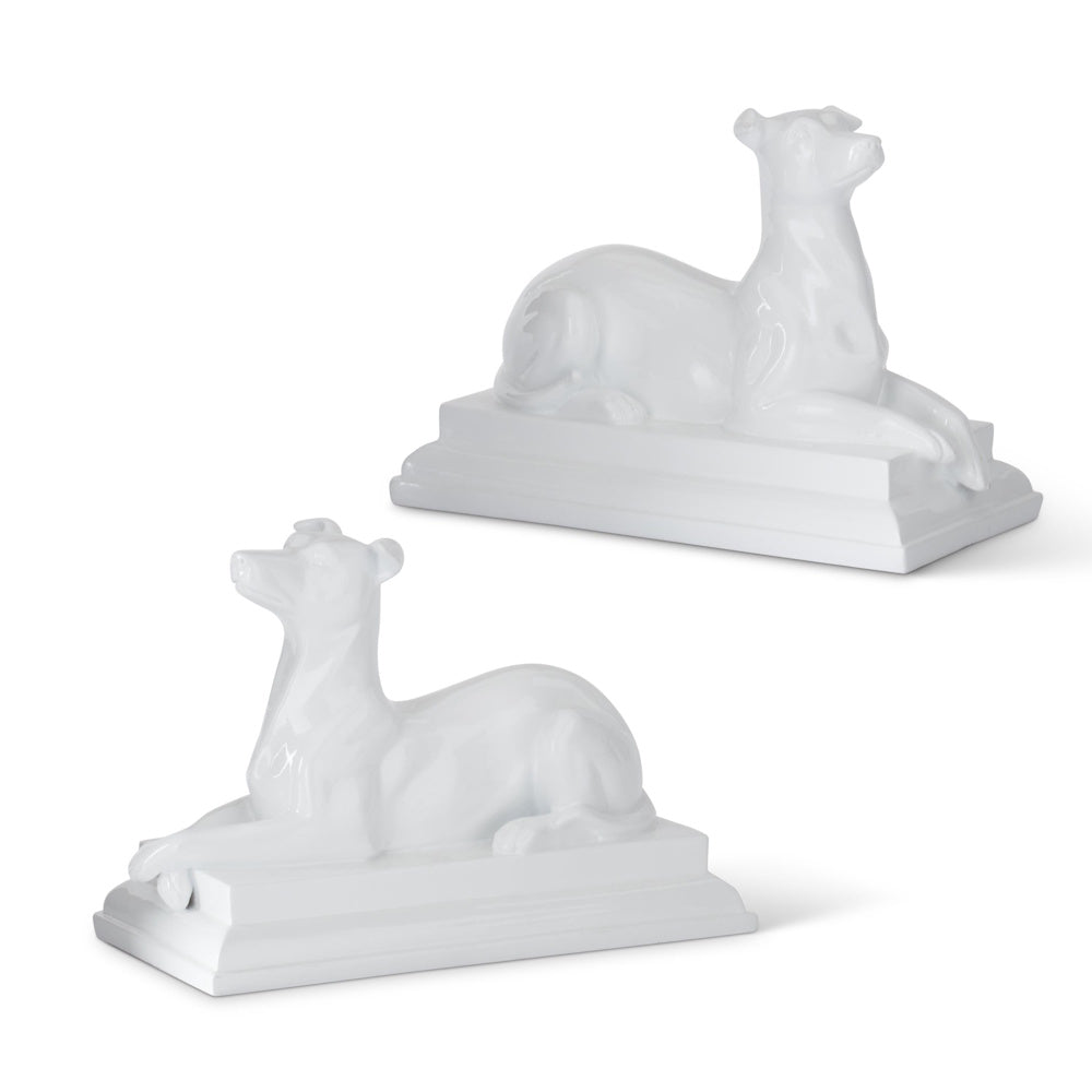 Pair of glossy white enameled resin dog statues on rectangular bases, facing opposite directions in a reclining pose.