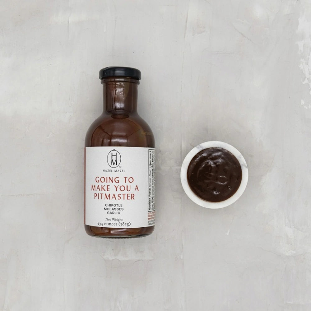 A bottle of Hazel Mazel Pitmaster sauce next to a small bowl of the dark brown chipotle molasses sauce.