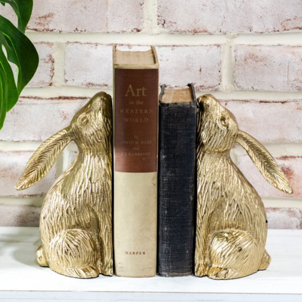 Pair of gold bunny bookends holding up two vintage books against a brick wall background.