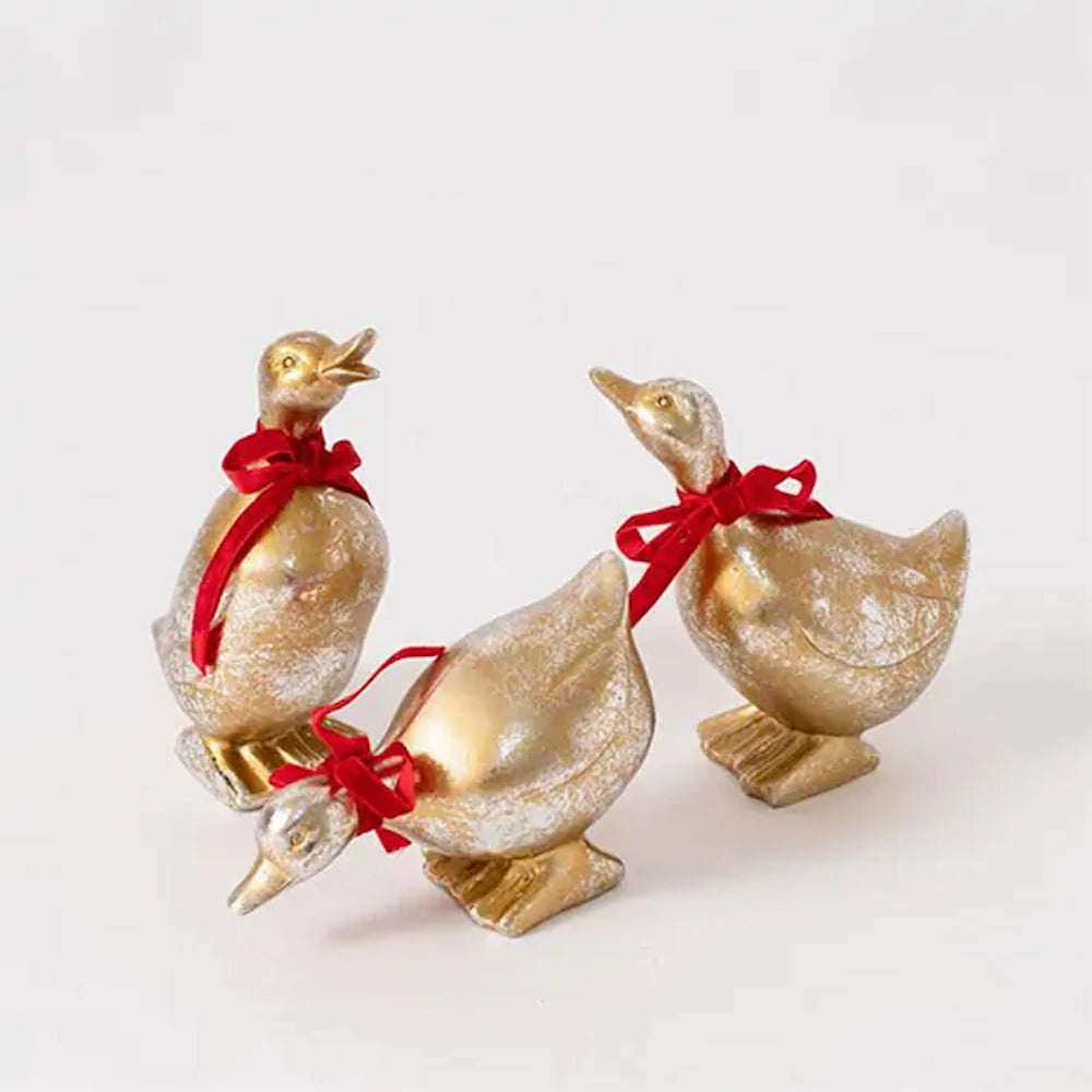 Three metallic gold duck figurines with red ribbon bows tied around their necks.