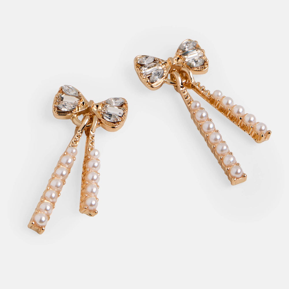 Gold bow dangle earrings featuring clear crystals on the bows and hanging strands inlaid with small white pearls.