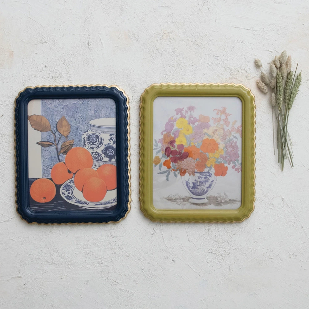 Two framed art prints with scalloped gold edges, featuring a still life of oranges and a floral bouquet in vases.
