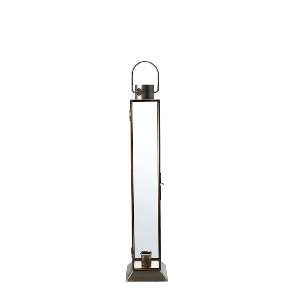 Tall, narrow gold metal and glass lantern with a top handle and internal taper candle holder on a square base.