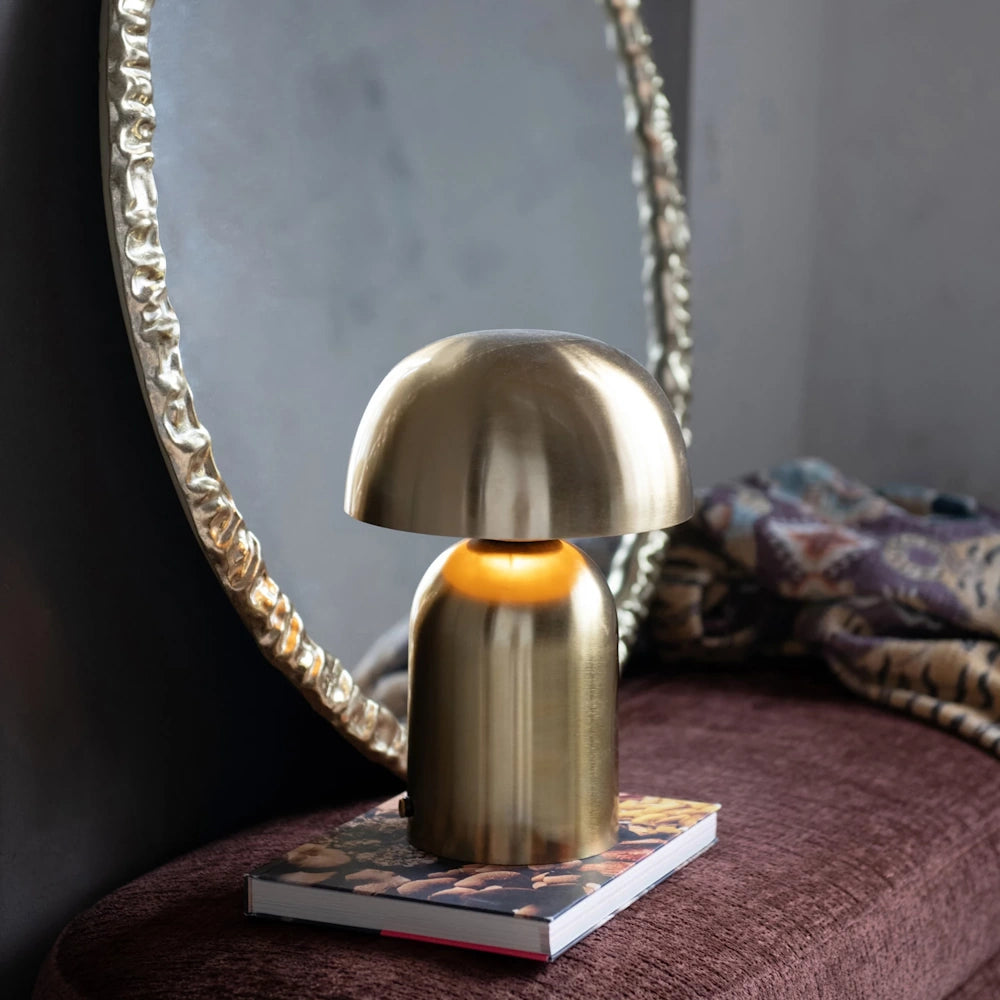 Modern gold mushroom lamp on a book in front of a textured gold-framed round wall mirror.