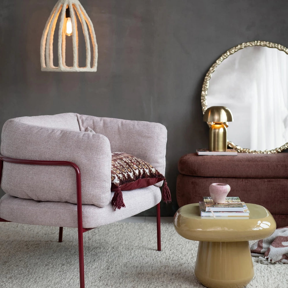 Round textured gold wall mirror in a modern living room with a pink armchair and a dark gray accent wall.