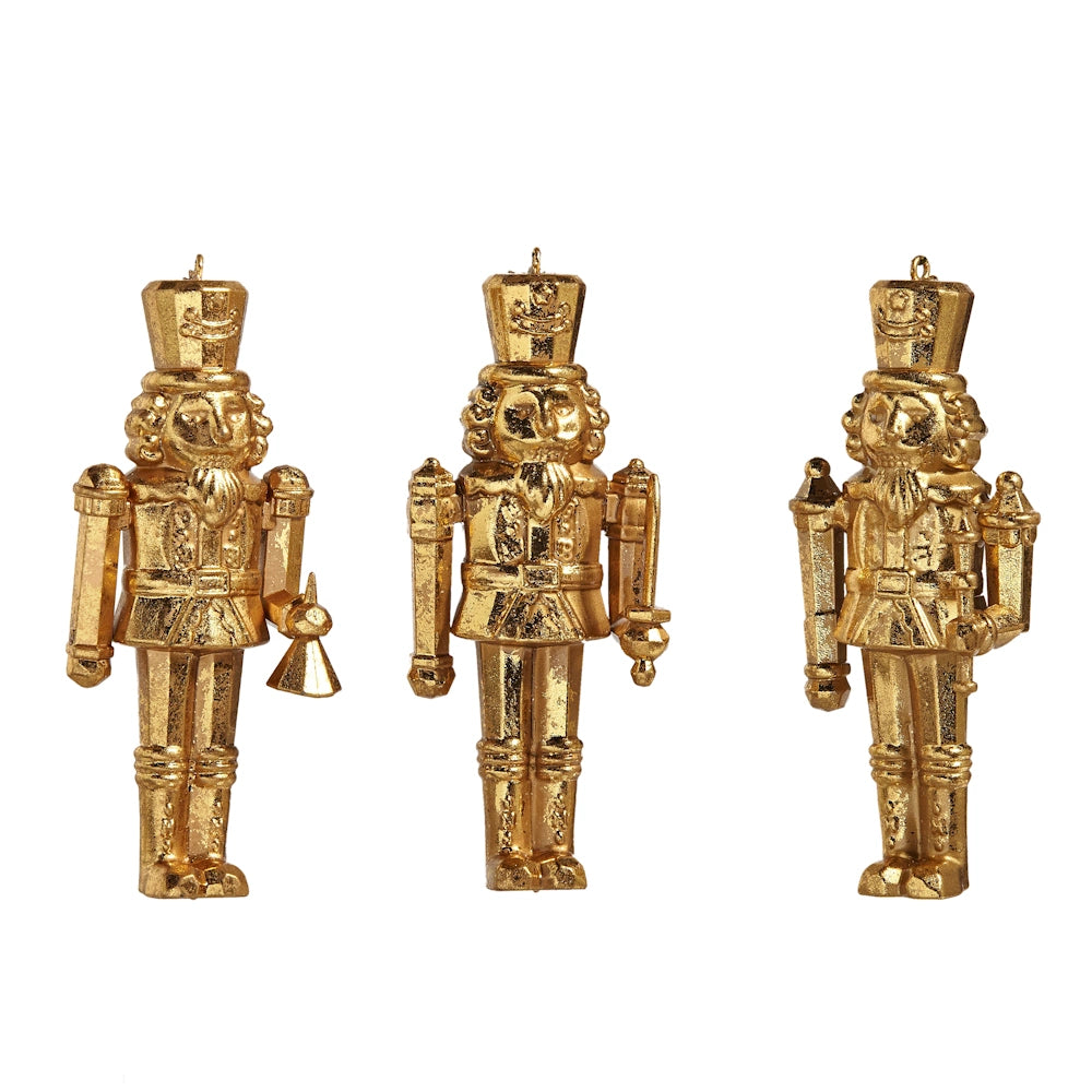 Three gold nutcracker Christmas tree ornaments with textured finishes holding different accessories.