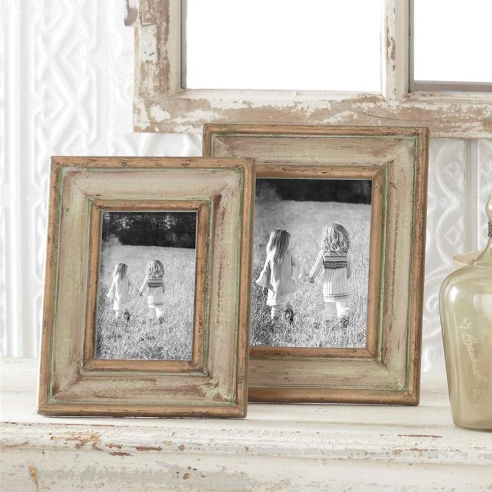 Two gold and green patina carved wood photo frames featuring black and white pictures on a rustic mantel.