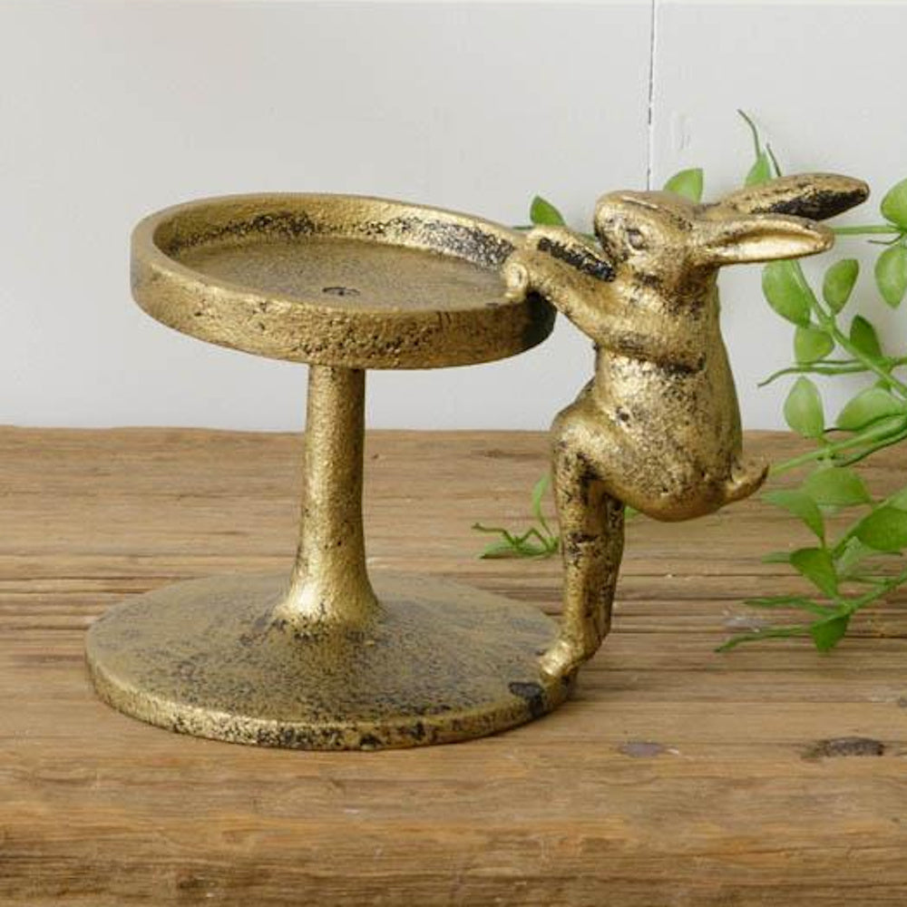 Antique gold rabbit pillar candle holder on a rustic wood surface, simple and direct home decor photography.