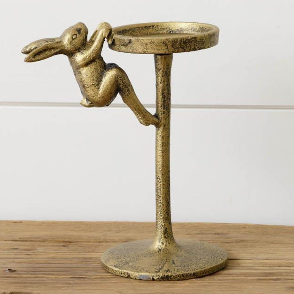 Gold bunny pillar candle holder with a textured antique finish, featuring a rabbit climbing a pedestal on a wood surface.