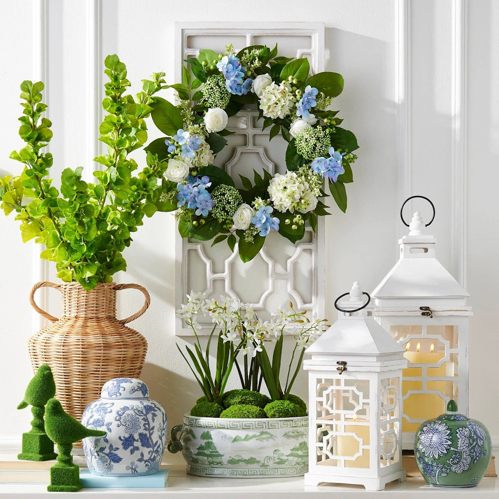 Spring-themed decor featuring a floral wreath, white lanterns, a wicker vase, and blue-and-white chinoiserie pottery.