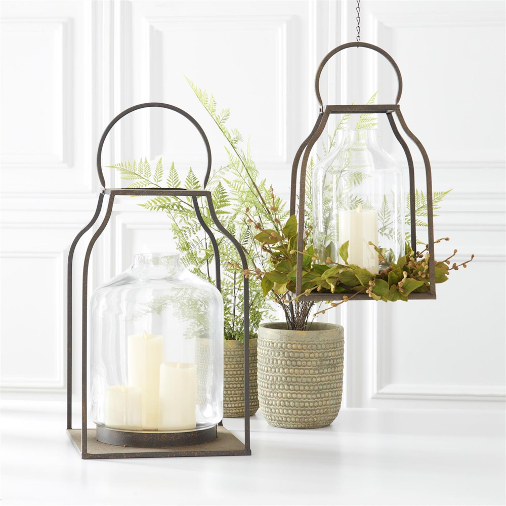 Two metal lanterns with glass hurricanes, pillar candles, and a green beech candle ring decoration.