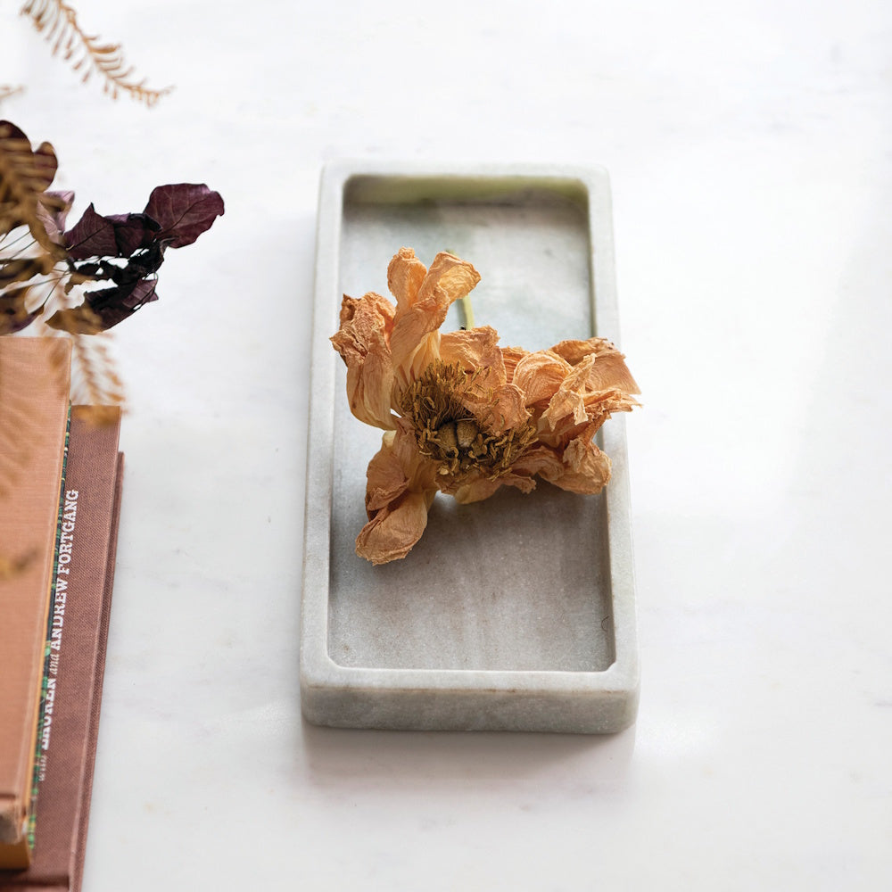 A dried orange flower resting inside a rectangular pale green marble tray.