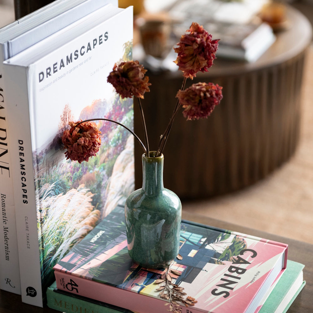 Small green glazed vase with dried flowers sitting on a stack of coffee table books.