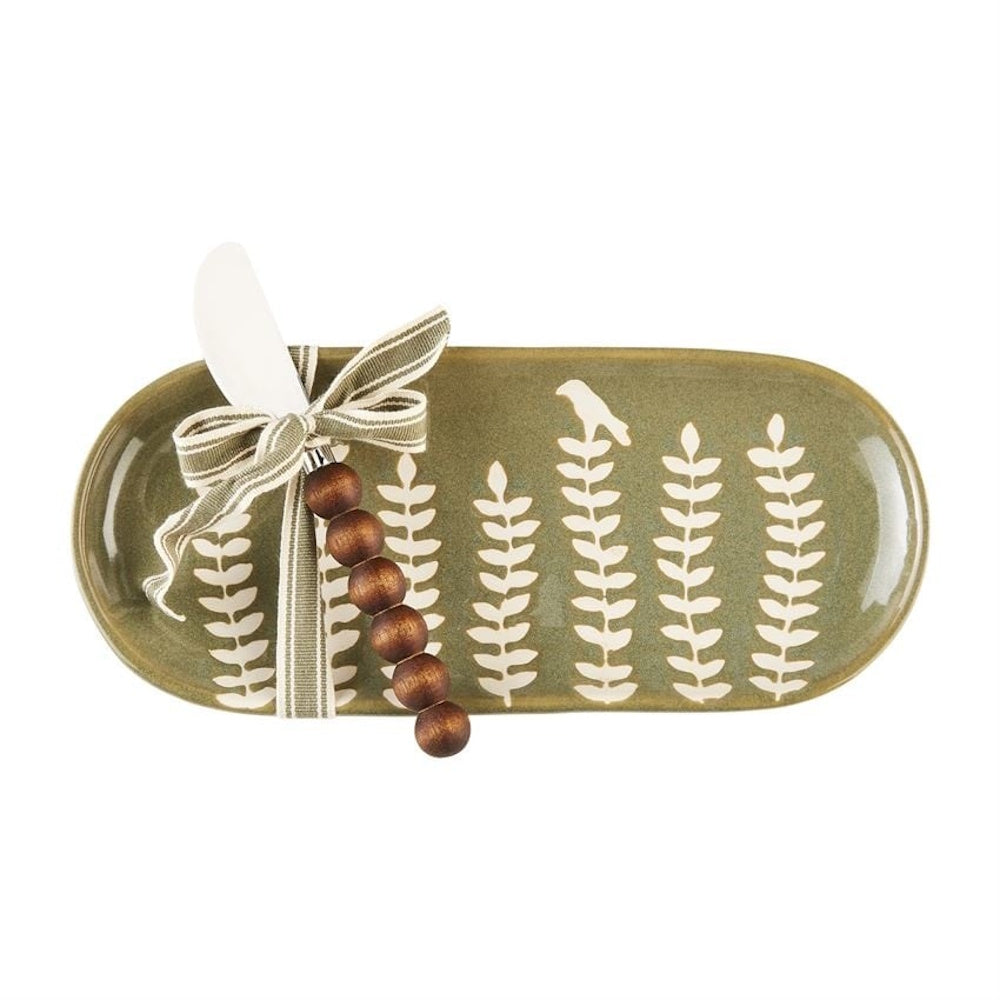 Green oval ceramic dish with white leaf patterns and a tied spreader knife featuring wooden beads.