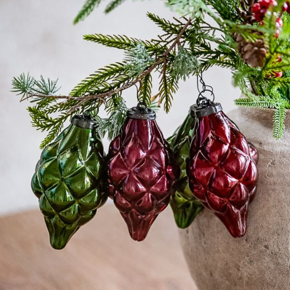 Set of four textured red and green glass drop ornaments hanging from a pine branch.