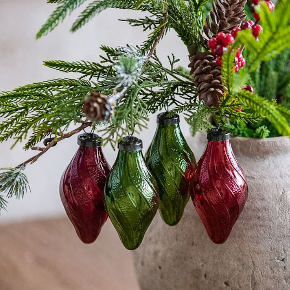 Set of four swirled red and green glass teardrop ornaments hanging from a pine branch.