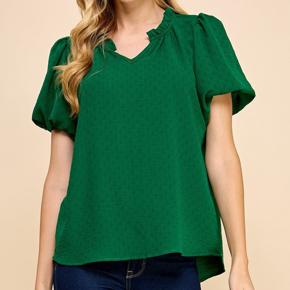 A woman wears a green, textured short-sleeve blouse with a ruffled split neckline and puff sleeves.