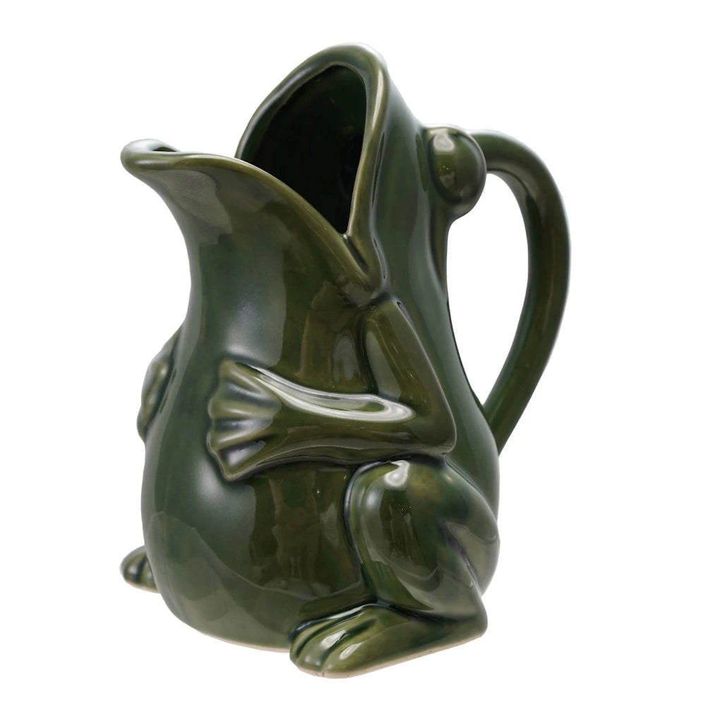 Glossy dark green stoneware pitcher shaped like a frog with an open mouth spout and curved handle on a white background.