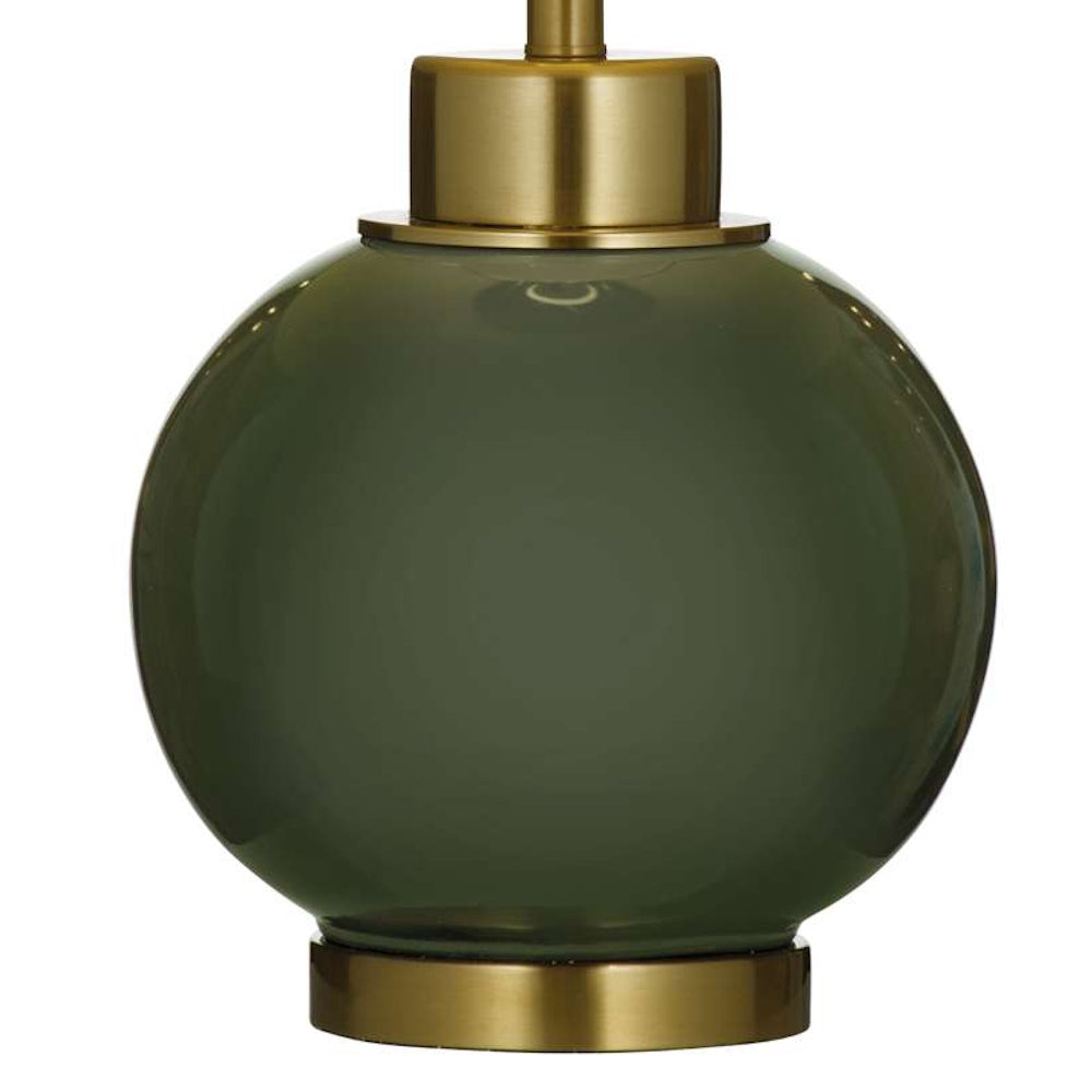 Close-up of a round olive green glass lamp base with brushed brass metal hardware at top and bottom.