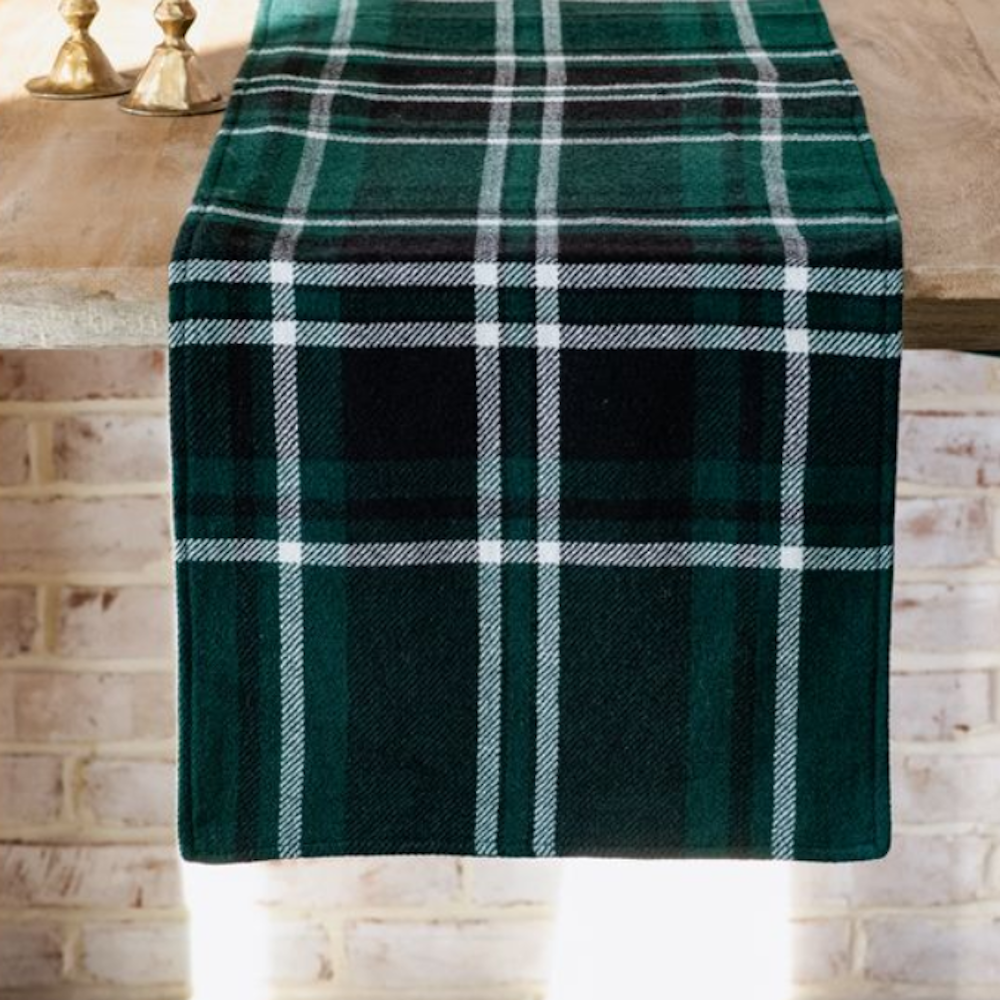 A green tartan plaid fabric table runner with white stripes draped over a wooden tabletop.