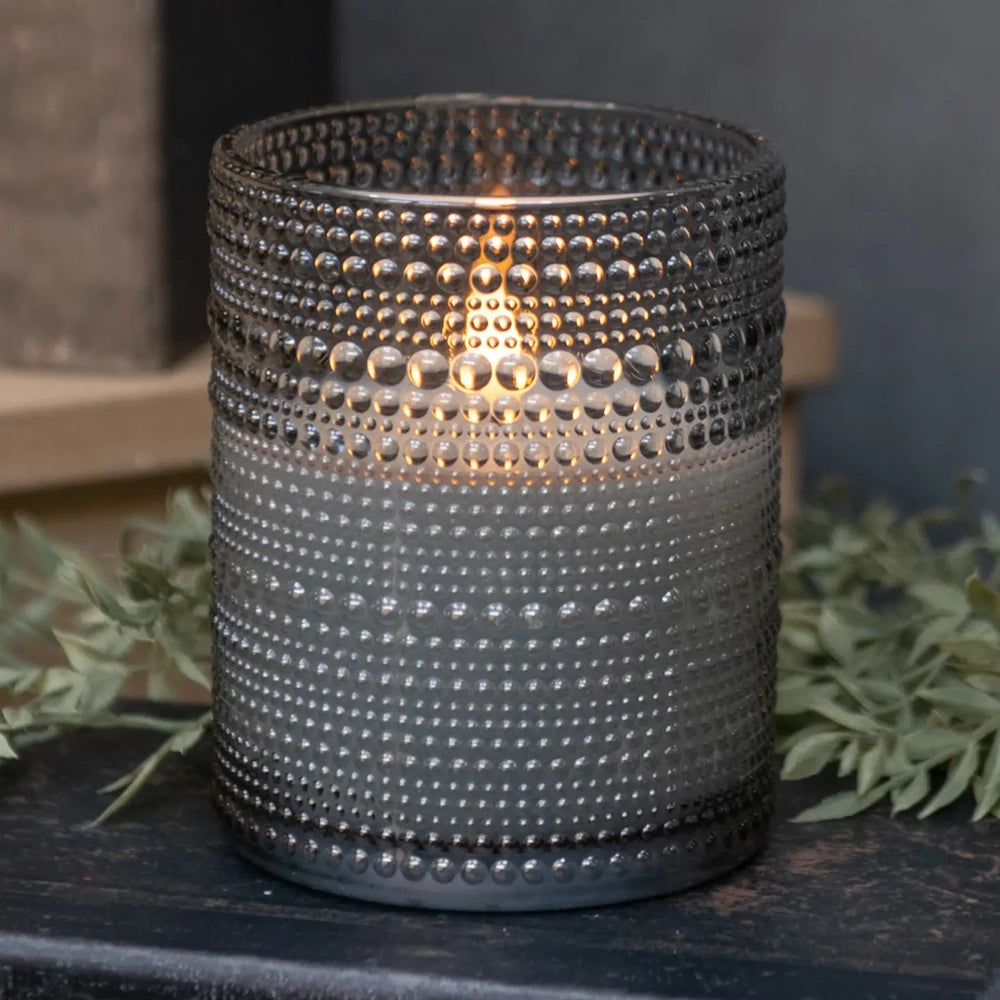 Grey dotted glass votive with a glowing 3D flameless candle inside, set on a dark surface.