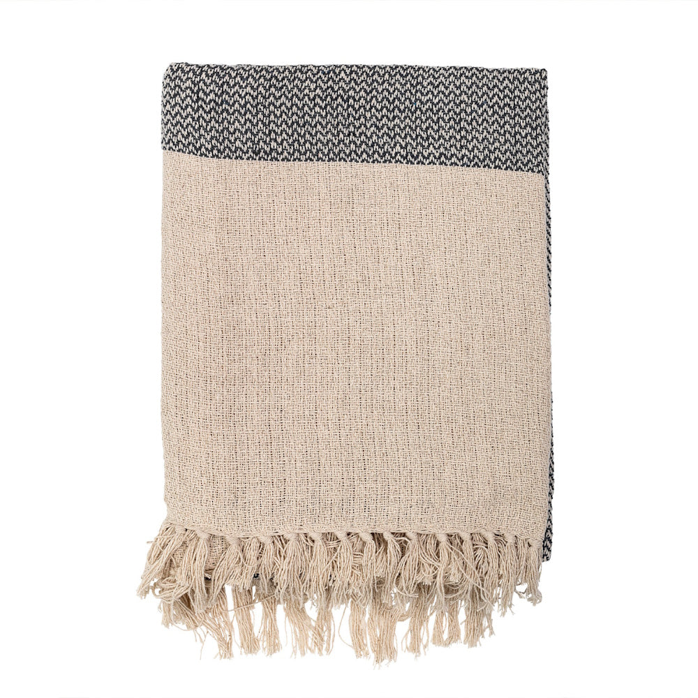 Folded knit throw blanket featuring a textured beige body, a dark grey patterned border, and knotted fringe.
