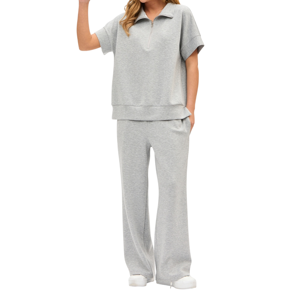 A woman wearing a grey short-sleeve quarter-zip top and matching wide-leg lounge pants with white sneakers.