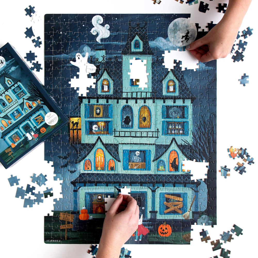 Hands assembling a Halloween haunted house jigsaw puzzle with ghosts, skeletons, and jack-o'-lanterns.