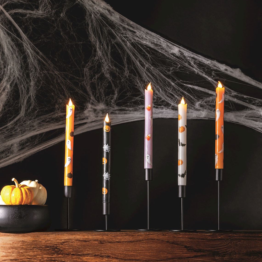 Five Halloween LED taper candles with spooky patterns lit on a mantel against a spiderweb background.