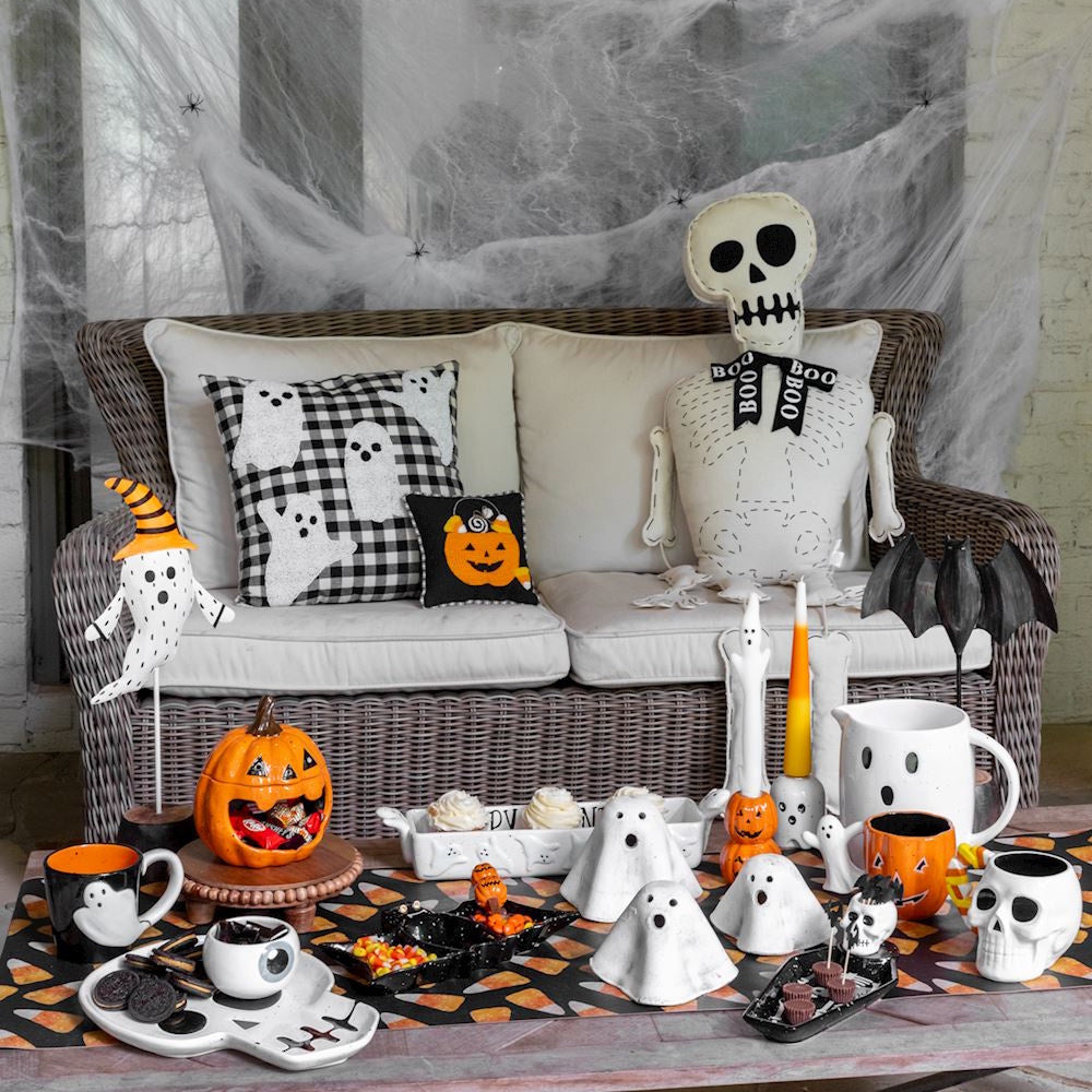 Halloween table decor with a pumpkin candy bowl, ghost figurines, and skeleton pillow.