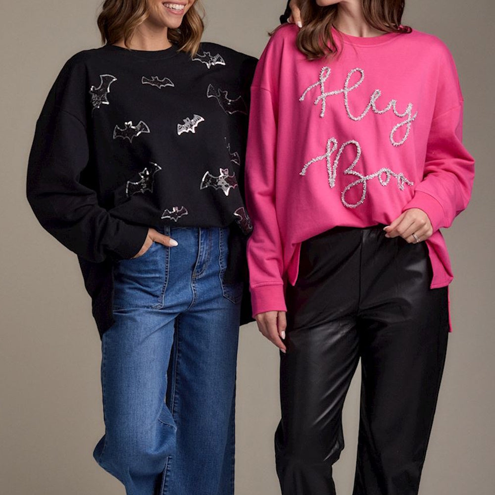 Women in Halloween sweatshirts: black with silver bats and pink with glittery "Hey Boo" text.