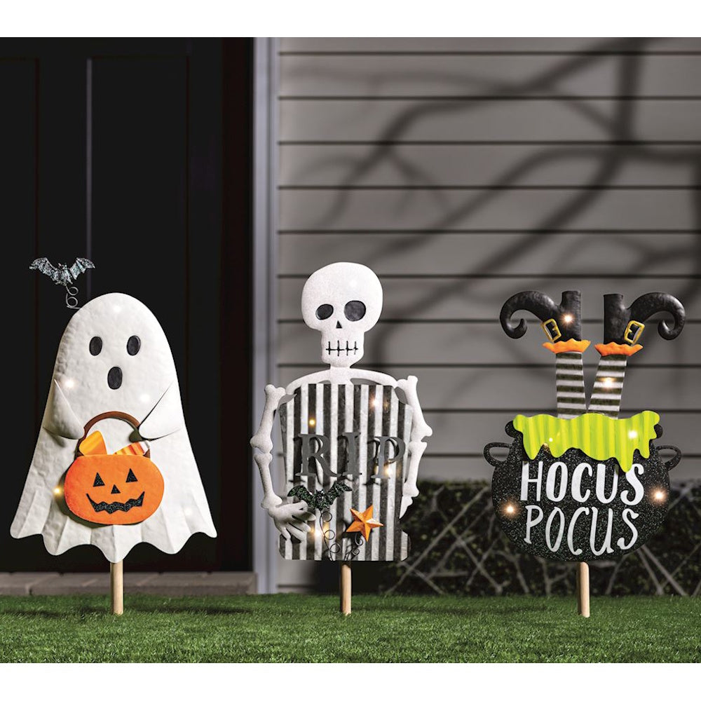 Three Halloween yard stakes: a ghost holding a pumpkin, a skeleton with a RIP sign, and a witch's cauldron.