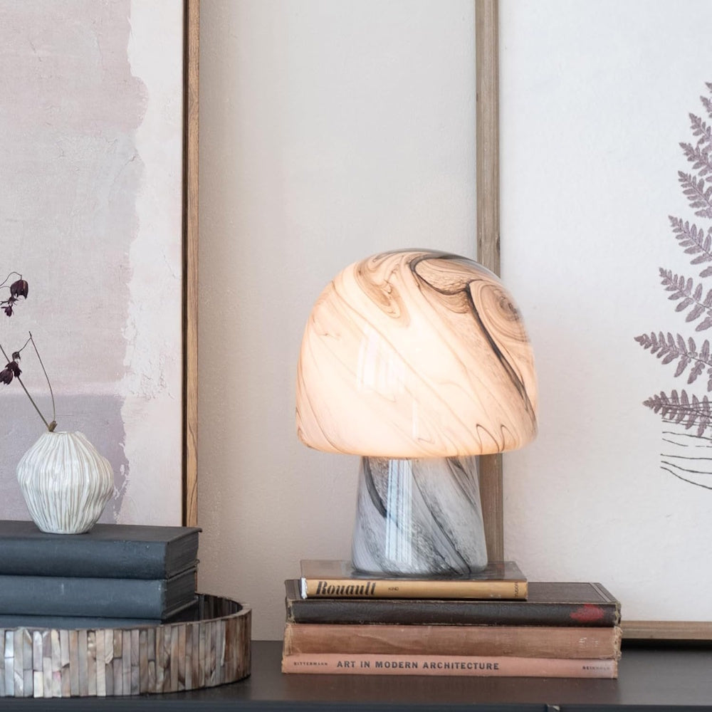 Hand-blown mushroom-shaped art glass table lamp with neutral marble swirl pattern on a stack of books.