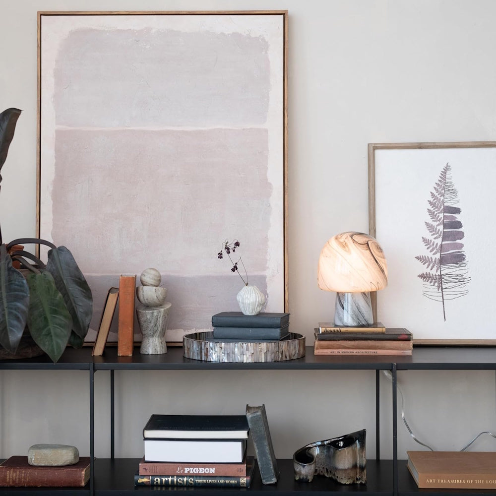 Hand-blown mushroom-shaped art glass table lamp with a marbled swirl pattern on a shelf with books and framed art.