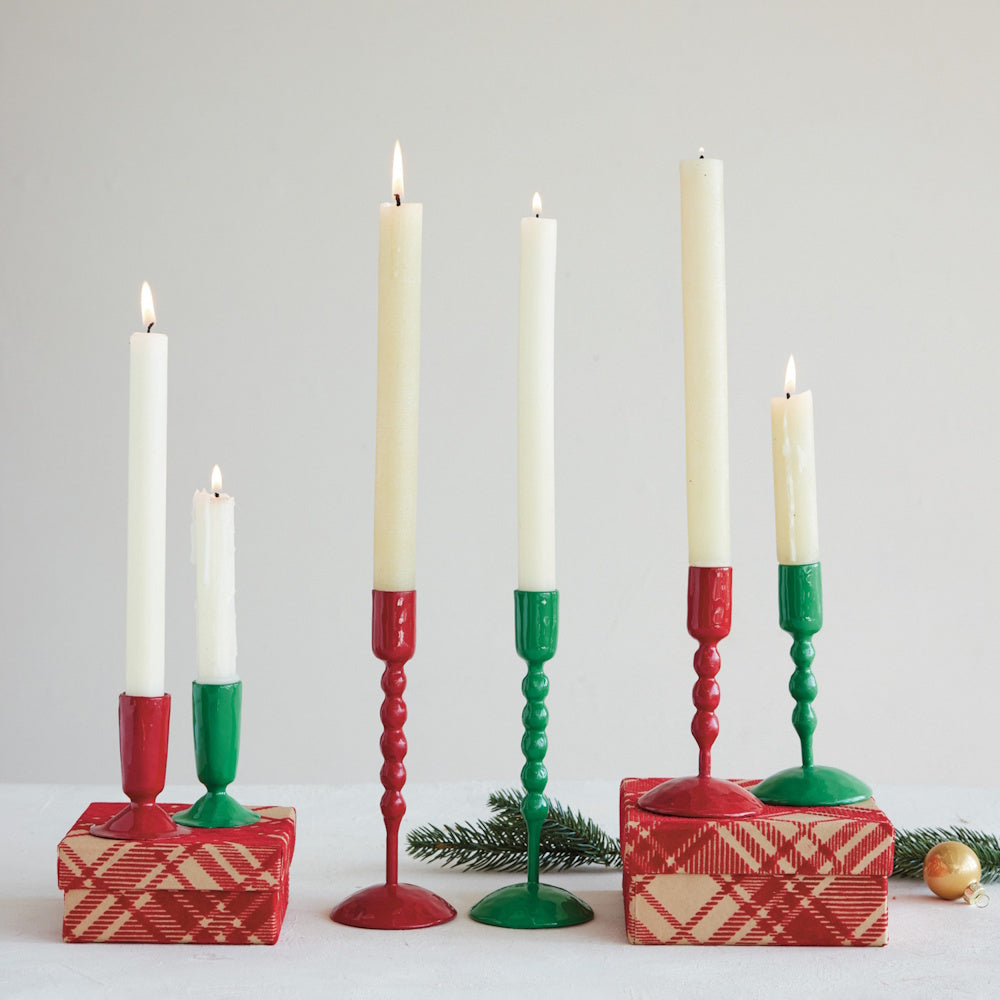 Red and green taper candle holders with lit white candles set on patterned gift boxes.