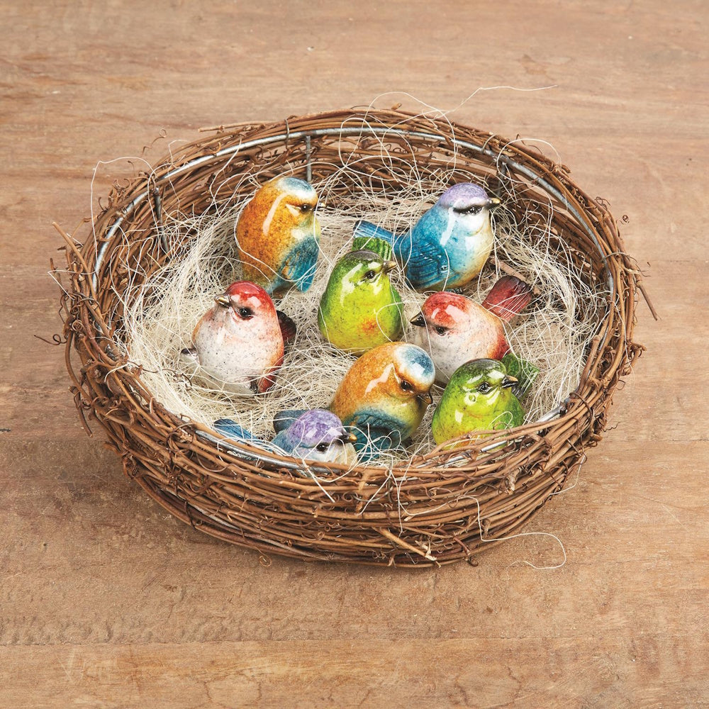 Colorful hand-painted ceramic bird figurines sitting inside a woven twig nest filled with sisal fiber.