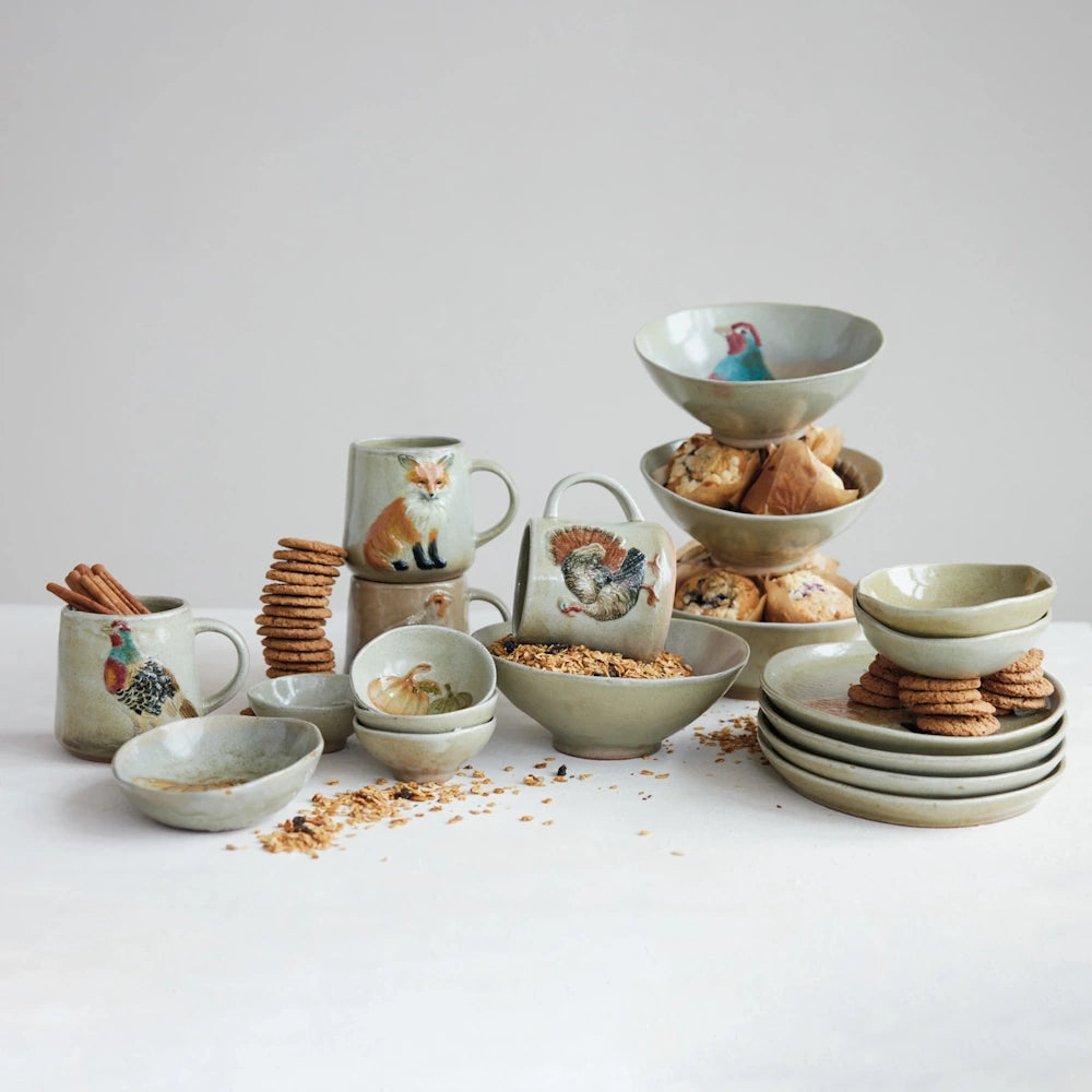 Animal-themed ceramic mugs arranged with cinnamon sticks, cookies, and spilled granola on a white surface.
