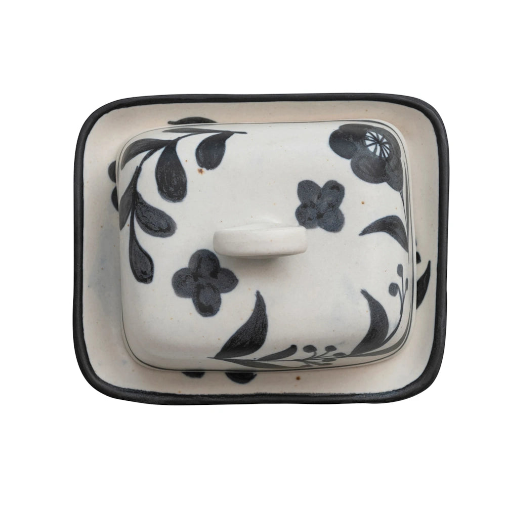 Top view of a hand-painted cream and black stoneware butter dish with a floral design.
