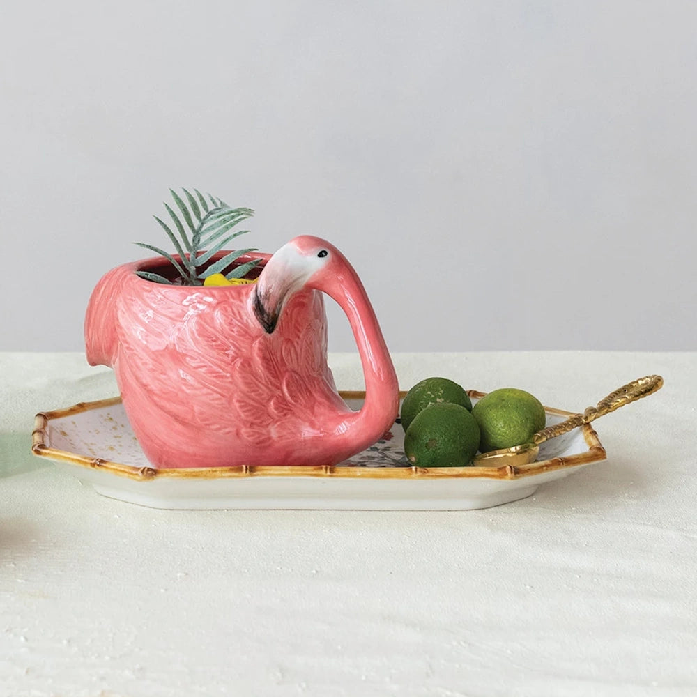 Hand-painted pink stoneware flamingo-shaped mug with a green plant on a decorative tray with limes and a gold spoon.