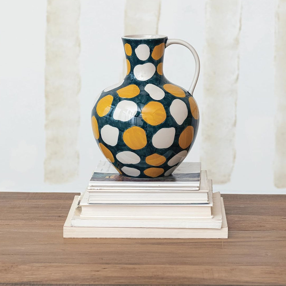Large polka dot ceramic pitcher sitting on a stack of books and a wooden table.