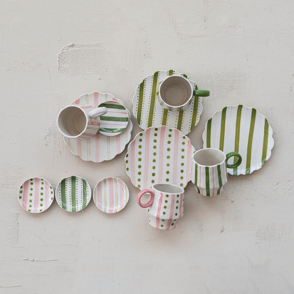 Hand-painted ceramic mugs, plates, and saucers in green and pink striped and dotted patterns.