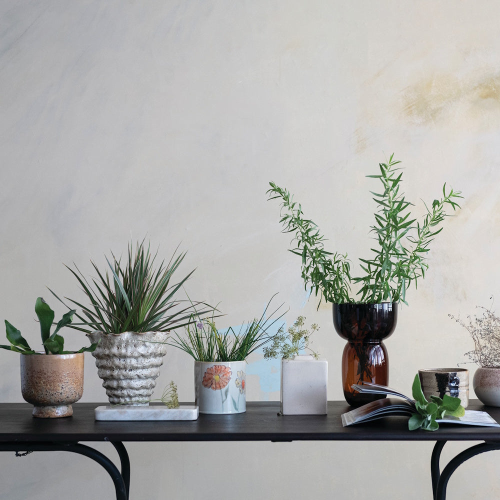 Hand-painted floral ceramic planter displayed alongside varied vases and potted plants on a black table.