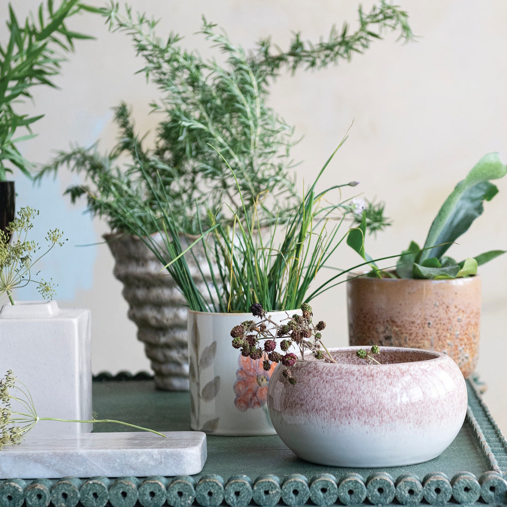 Close-up of a hand-painted floral ceramic planter and decorative pottery arranged on a table.