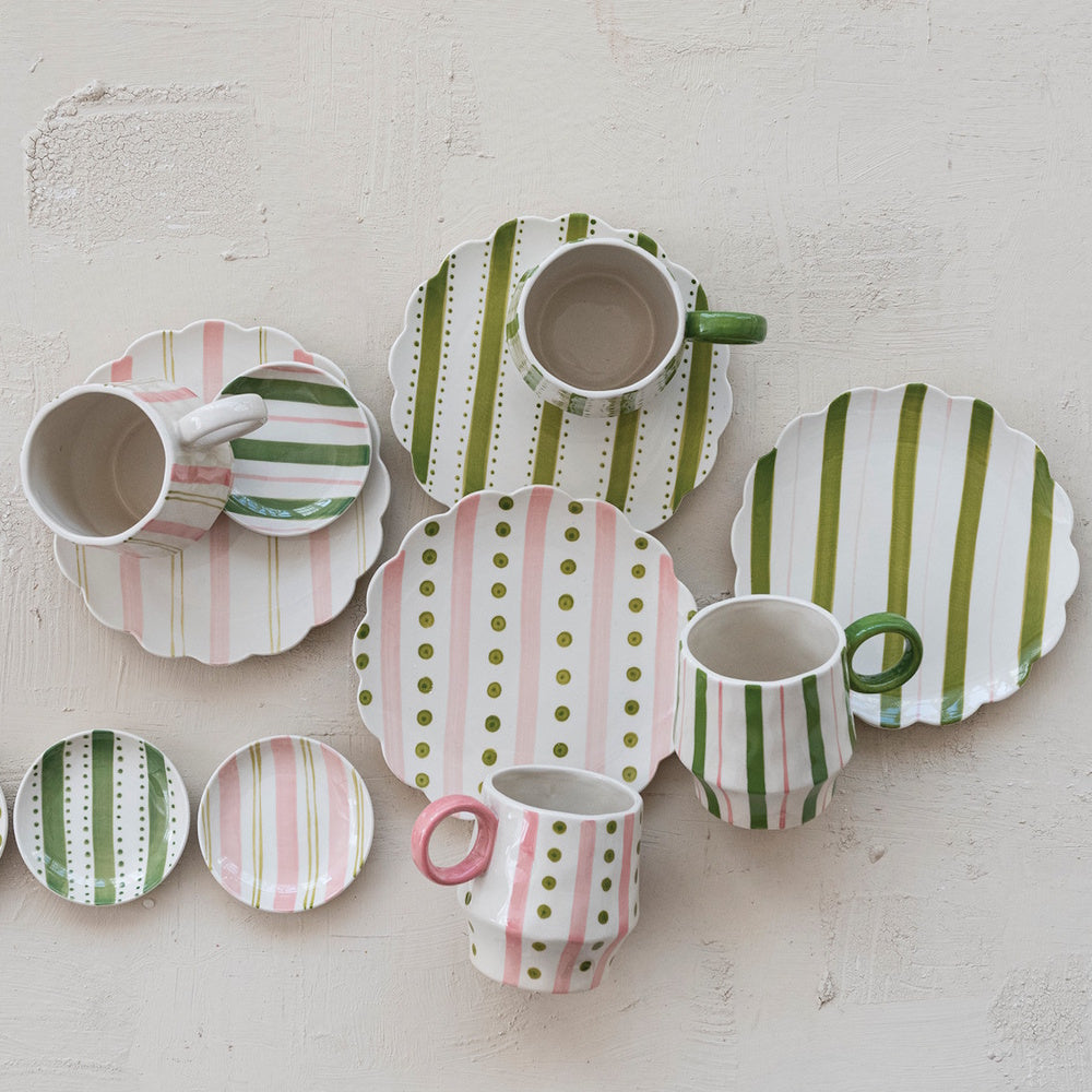 Flat lay of hand-painted ceramic mugs, plates, and small dishes with green and pink patterns.